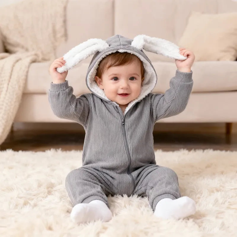Bébé souriant en barboteuse grise avec capuche et oreilles de lapin 3D assis sur un tapis"