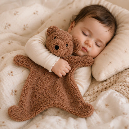 Bébé endormi tenant son doudou ours marron tout doux.