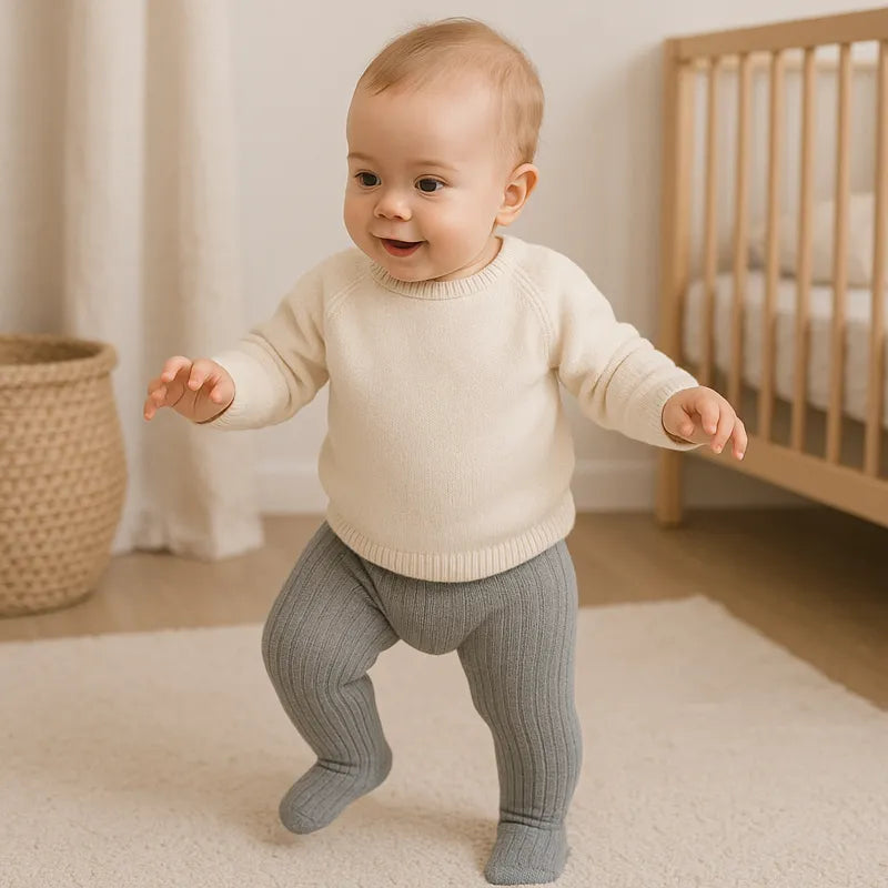 Bébé debout en train de marcher portant des collants gris doux et confortables dans une chambre beige