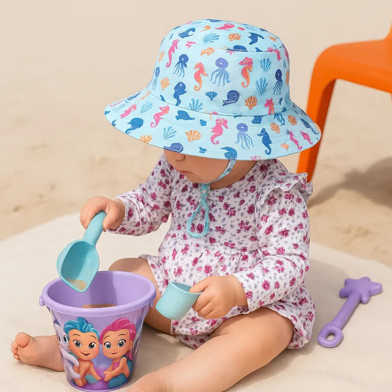Bébé sur la plage avec chapeau bleu imprimé animaux marins.