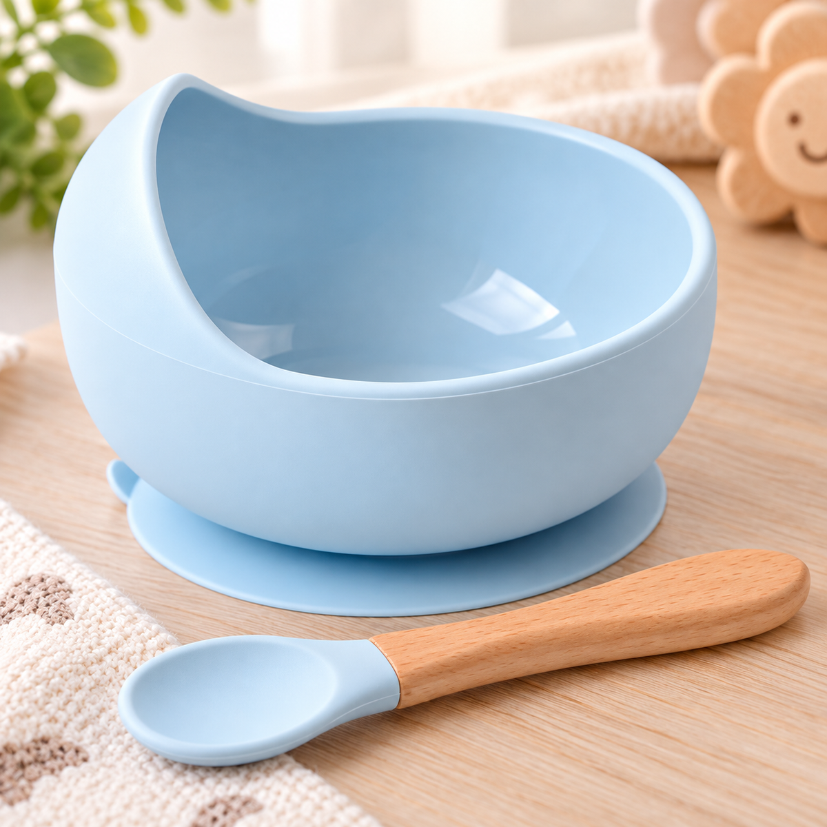 Bol en silicone bleu pour bébé avec base à ventouse et cuillère assortie à manche en bois, posé sur une table en bois clair.