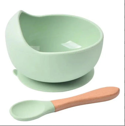 Bol en silicone vert pastel pour bébé avec rebord surélevé et base à ventouse, accompagné d'une cuillère verte à manche en bois
