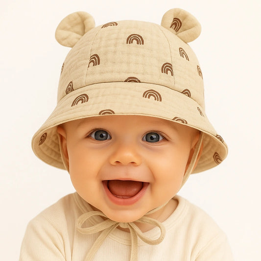 Bébé souriant portant un chapeau beige à motifs arc-en-ciel