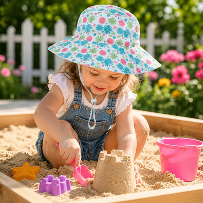 Petite fille portant un chapeau bébé anti-UV fleuri jouant dans un carré de sable
