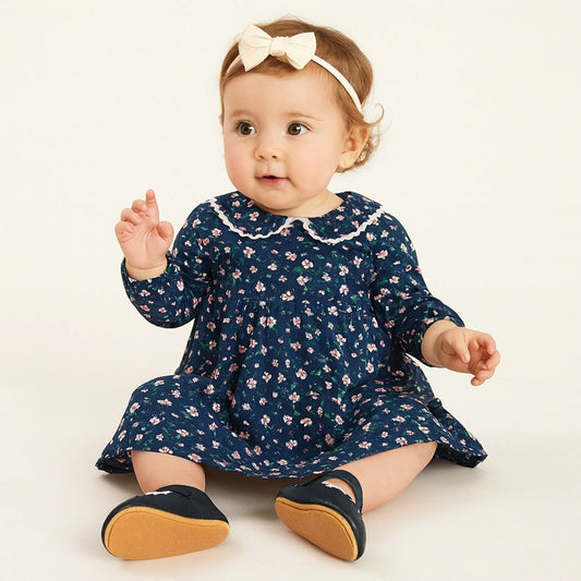 Bébé fille assise en robe fleurie bleue portant des chaussures noires en cuir souple