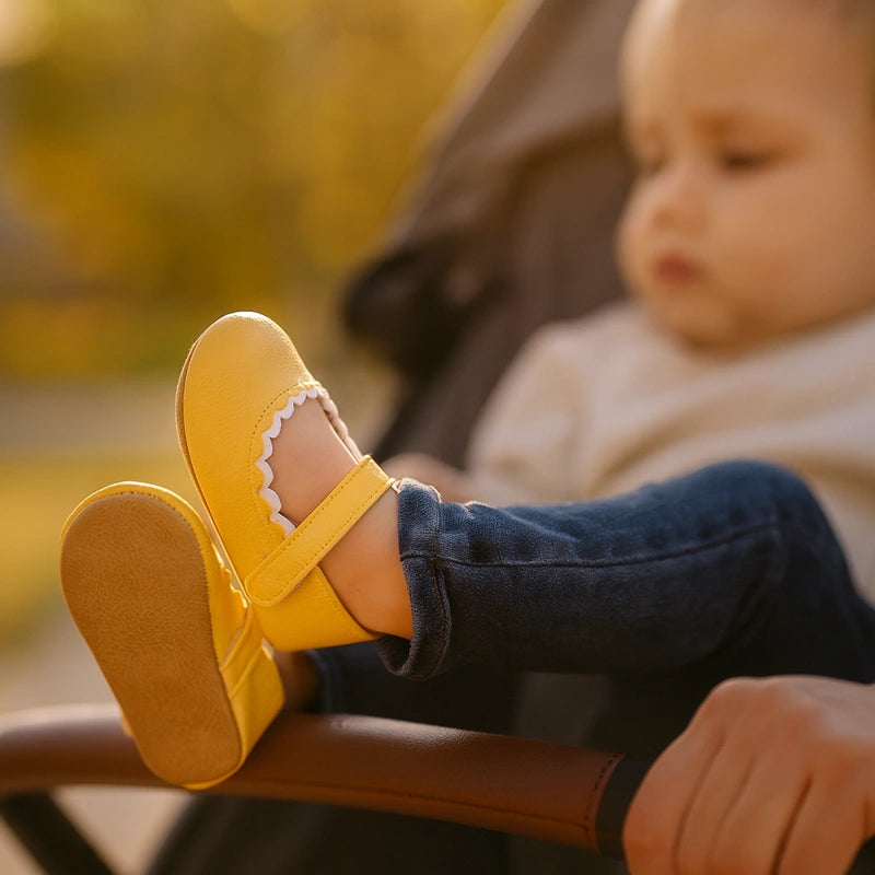 Bébé en promenade avec chaussures jaunes en cuir souple dans une poussette au soleil