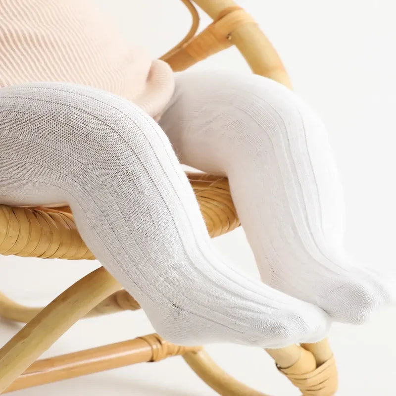 Jambes de bébé assis portant des collants bébé blancs doux et confortables sur chaise en rotin