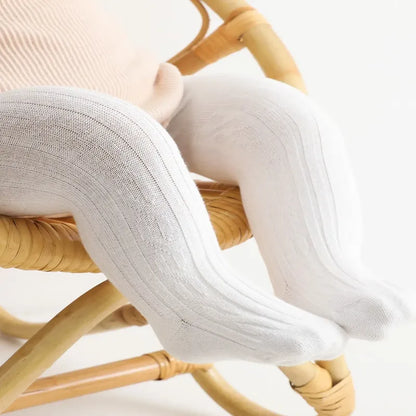 Jambes de bébé assis portant des collants bébé blancs doux et confortables sur chaise en rotin