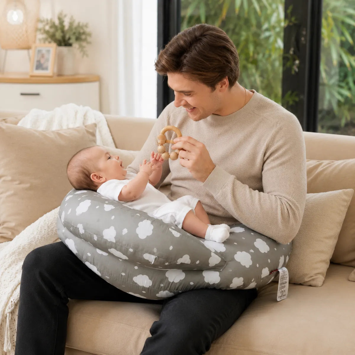 Papa jouant avec bébé sur un coussin d’allaitement gris avec hochet