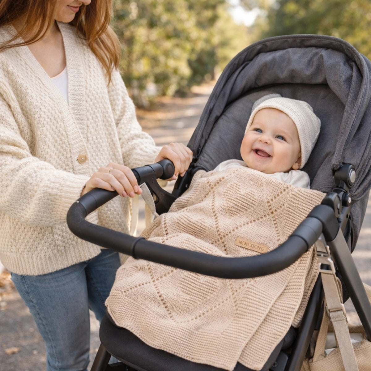 Bébé souriant dans une poussette, enveloppé dans une couverture bébé en tricot beige