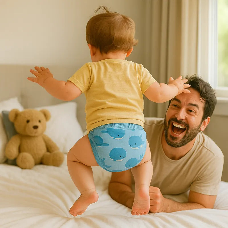 Bébé en culotte d’apprentissage bleue baleines sautant sur lit avec papa