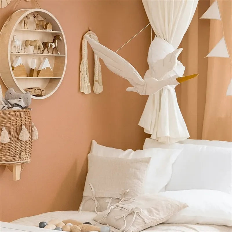 Cygne en peluche suspendu au-dessus du lit bébé, décoration murale bohème dans des tons crème et terracotta.