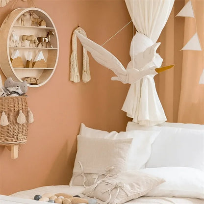 Cygne en peluche suspendu au-dessus du lit bébé, décoration murale bohème dans des tons crème et terracotta.
