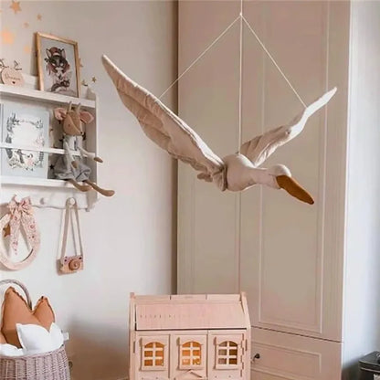 Décoration murale cygne en peluche suspendue au-dessus d’une maison miniature dans une chambre d’enfant beige et bois.