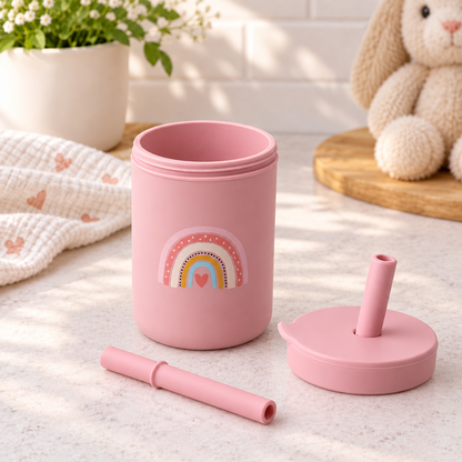 Tasse bébé silicone rose avec paille démontée, motif arc-en-ciel et éléments vue éclatée sur comptoir de cuisine