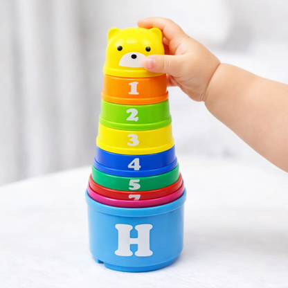 Gros plan sur une tour de gobelets empilables pour bébé, avec des chiffres colorés et une tête d'ourson jaune au sommet.