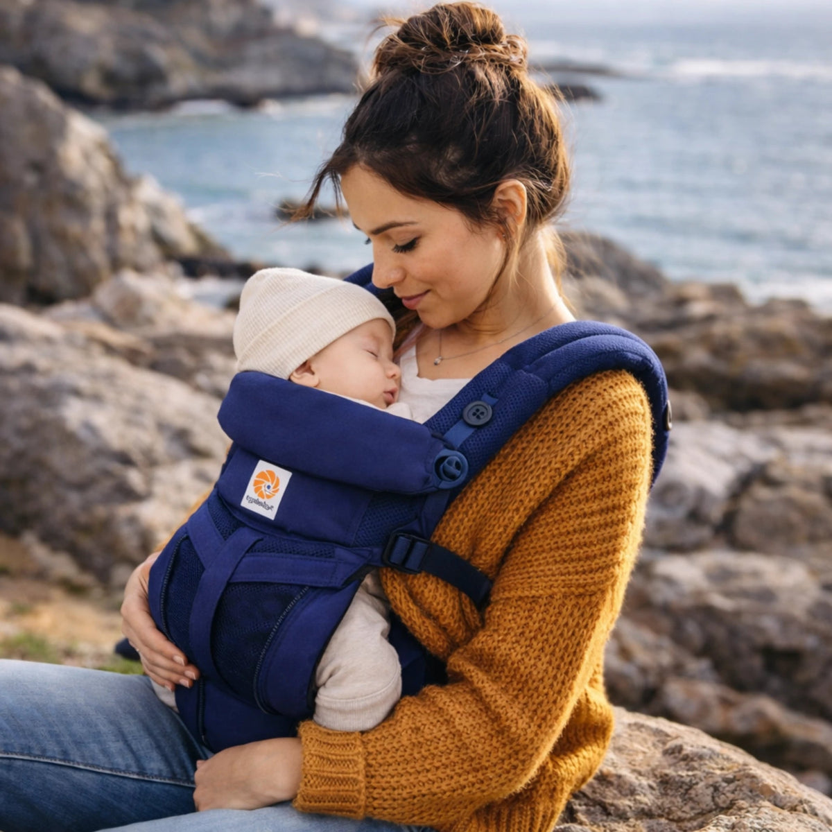 Bébé endormi dans porte-bébé ergonomique respirant porté par maman en extérieur bord de mer