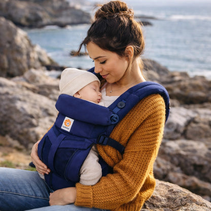 Bébé endormi dans porte-bébé ergonomique respirant porté par maman en extérieur bord de mer