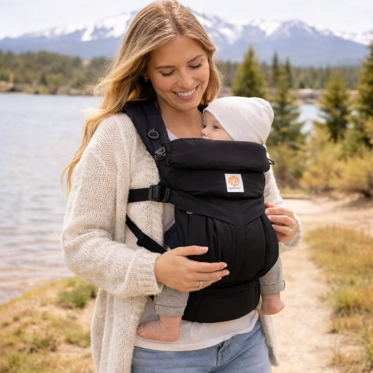 Maman portant bébé avec porte-bébé ergonomique confortable en extérieur près d’un lac paysage naturel