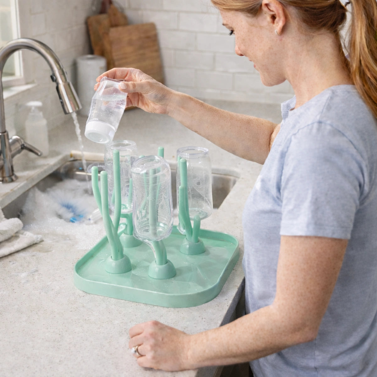 Séchoir biberon bébé compact avec bouteilles retournées sur support de séchage, maman nettoyant des biberons
