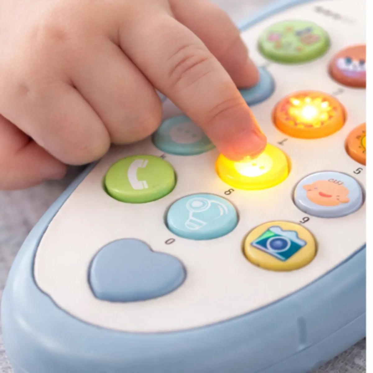 Main de bébé appuyant sur le bouton lumineux d’un téléphone jouet éducatif pour éveil sensoriel