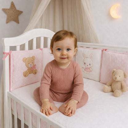 Bébé assis dans un lit bébé avec tour de lit rose en coton,