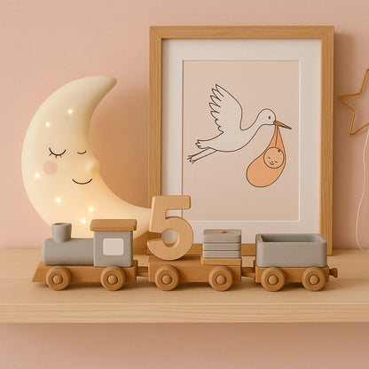 Train en bois décoratif posé sur une étagère dans une chambre de bébé rose poudré avec veilleuse lune et cadre cigogne.