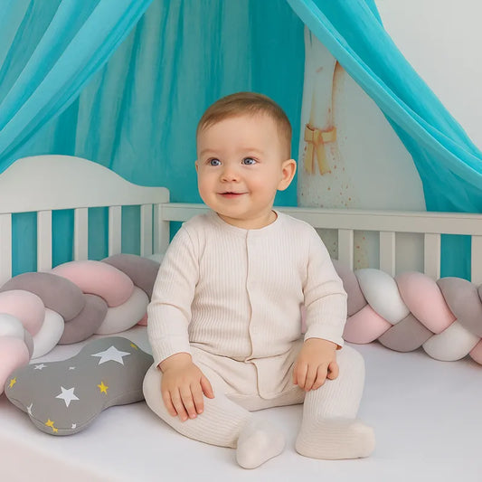 Tresse de lit bébé rose et grise avec bébé assis dans un berceau 