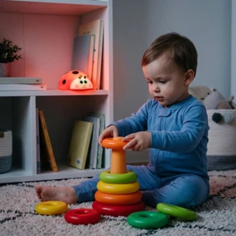 Bébé jouant dans sa chambre avec une veilleuse coccinelle LED allumée en arrière-plan.