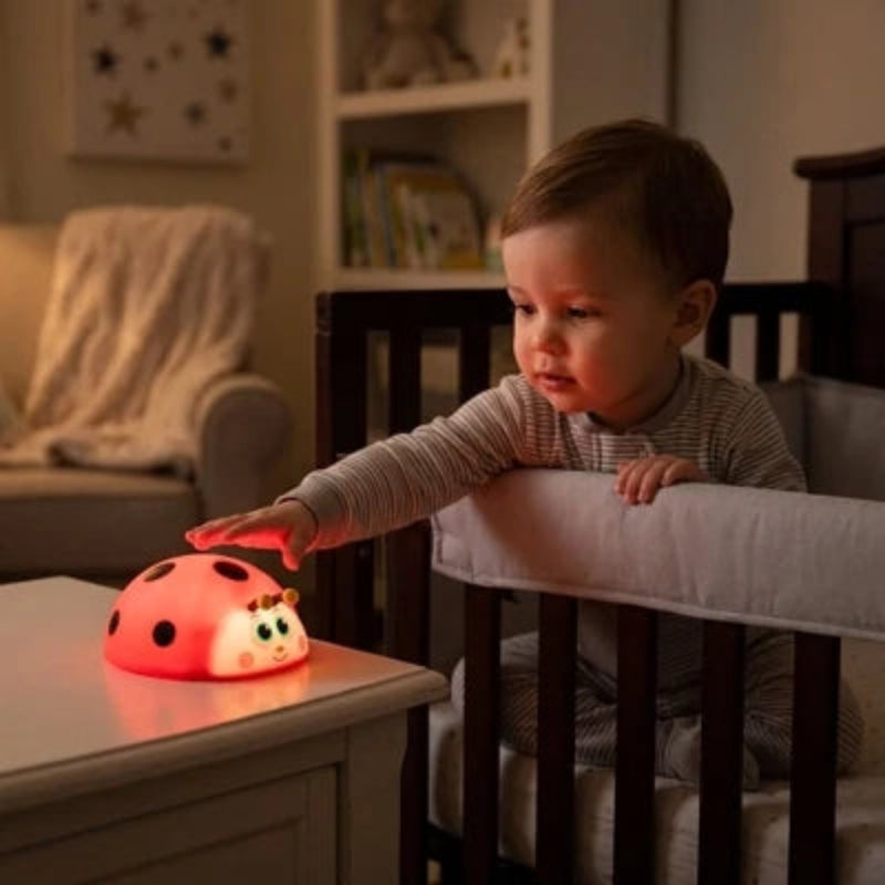 Bébé touchant une veilleuse coccinelle LED rechargeable posée sur la table de chevet de sa chambre.