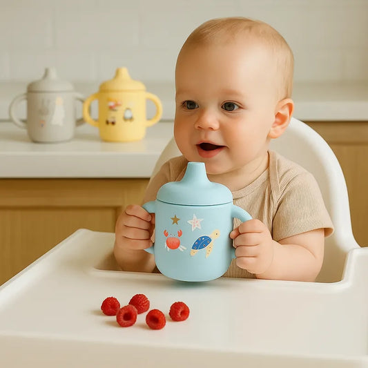 Bébé assis tenant une tasse en silicone bleu anti-fuite
